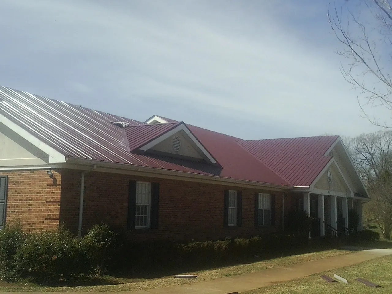 Red metal roof with gabled entries on a long brick building, from a Hail Damage Roof Repair job in Brunswick